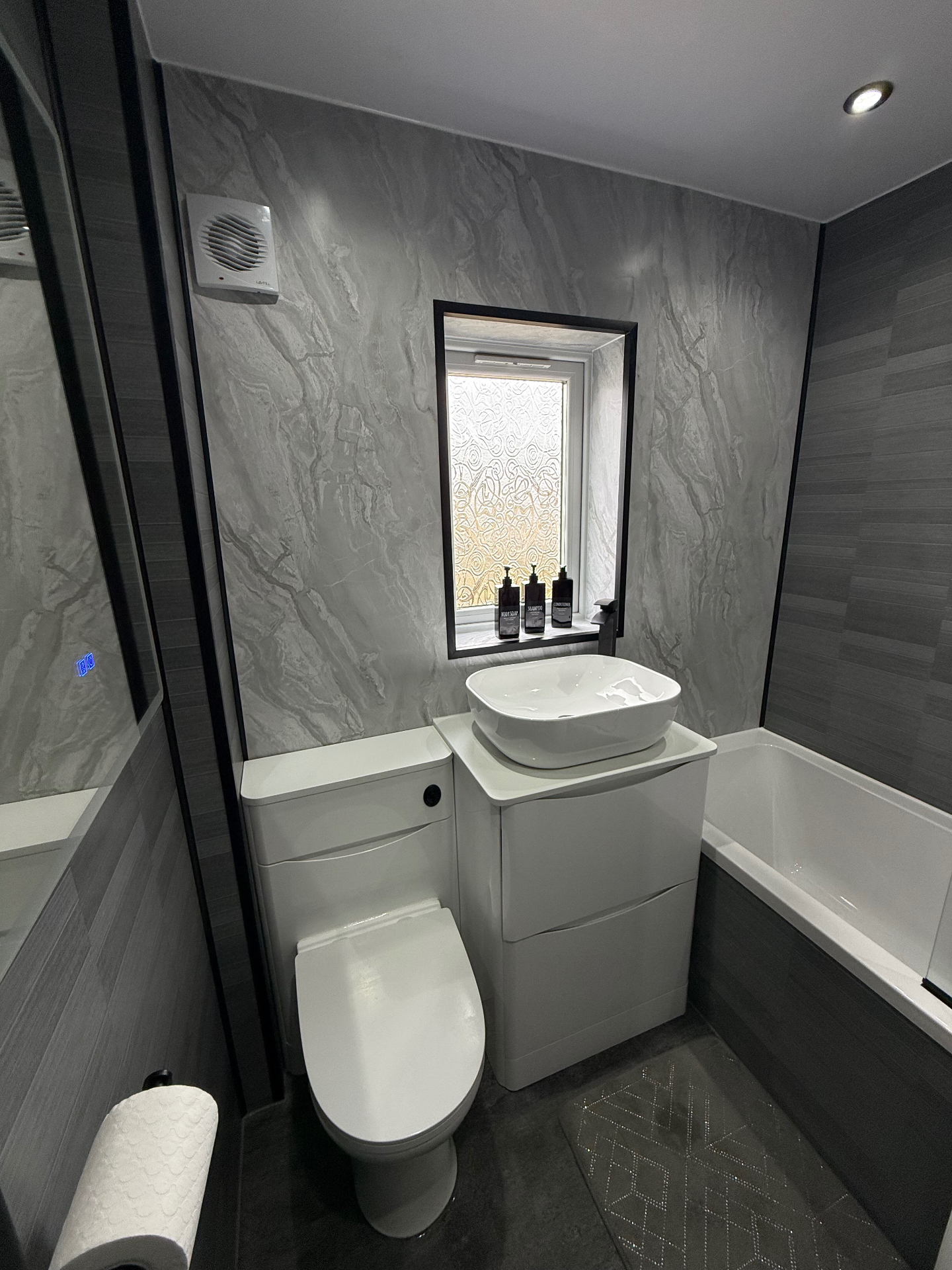 Stunning marble-effect wet wall bathroom with freestanding bath, backlit round mirror and white designer fixtures